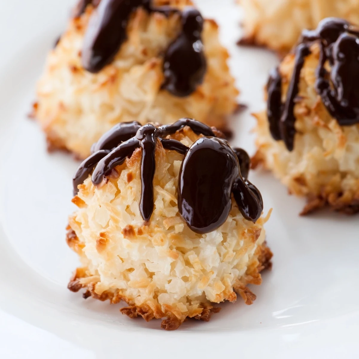 Golden-baked Coconut Macaroons with chocolate drizzle on a white plate, next to a cup of coffee.