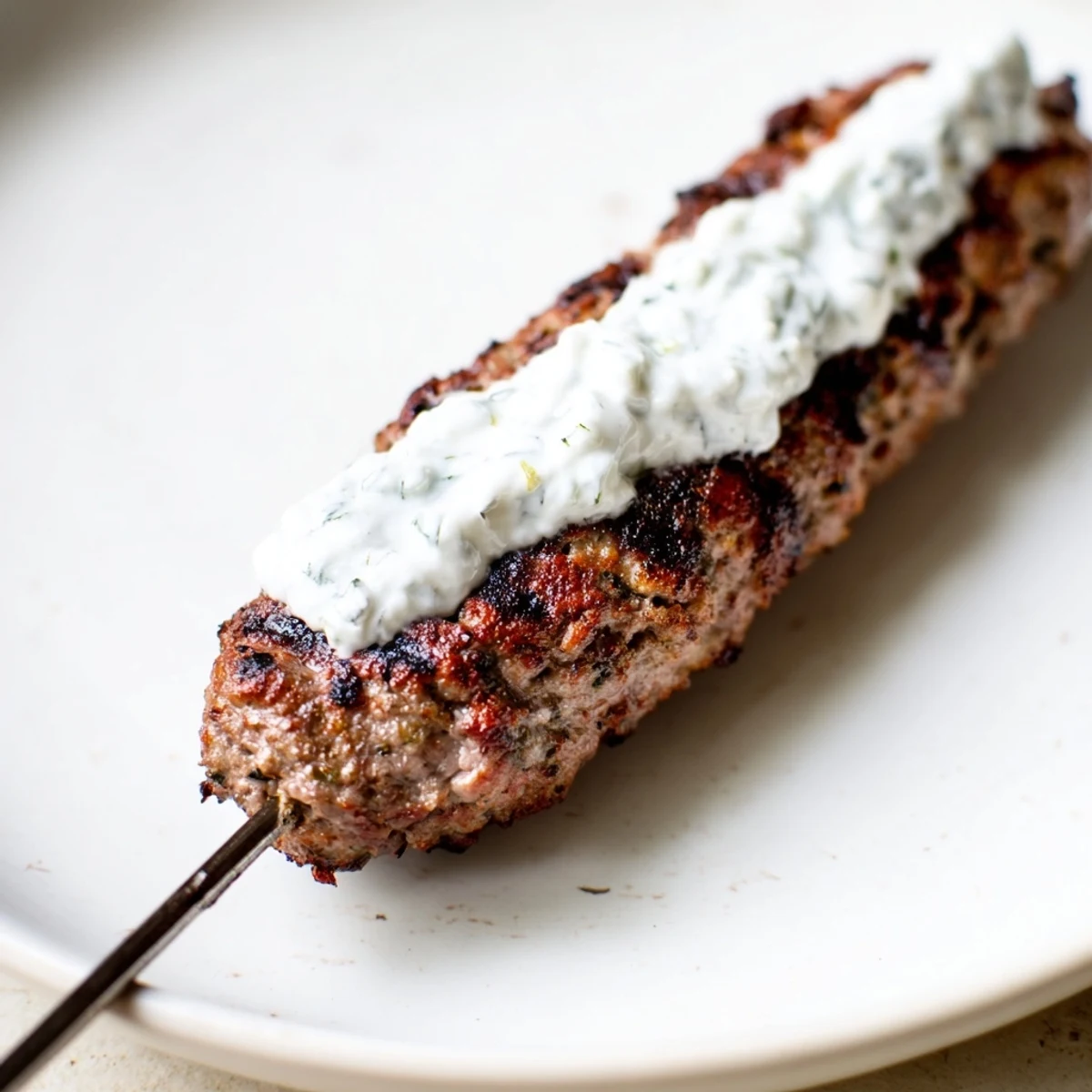 Freshly grilled Beef Kofta Kebabs with Tzatziki Sauce rest on a platter with warm pita bread and lemon wedges, ready to serve.