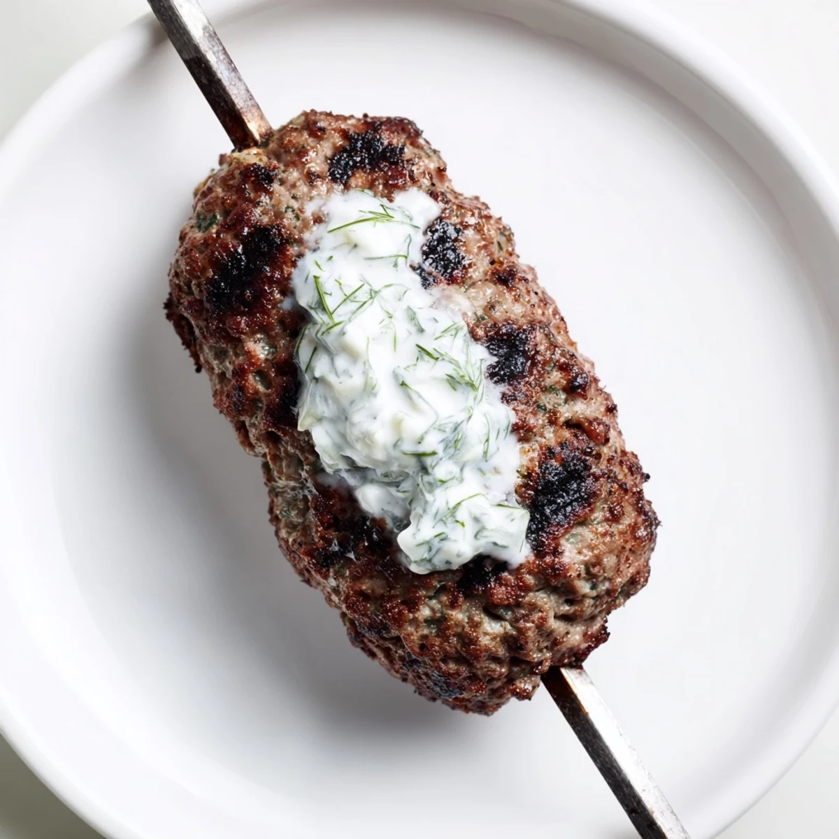 Overhead view of plated Beef Kofta Kebabs with Tzatziki Sauce, garnished with diced tomatoes, red onion, and chopped parsley.