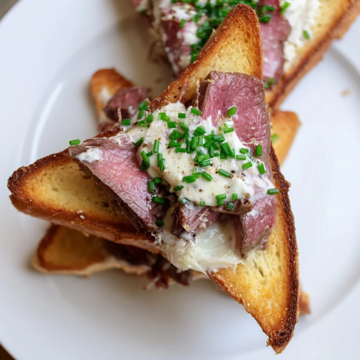 Golden, crispy Beef Toast Points topped with tender seared beef and creamy horseradish sauce on a serving plate.