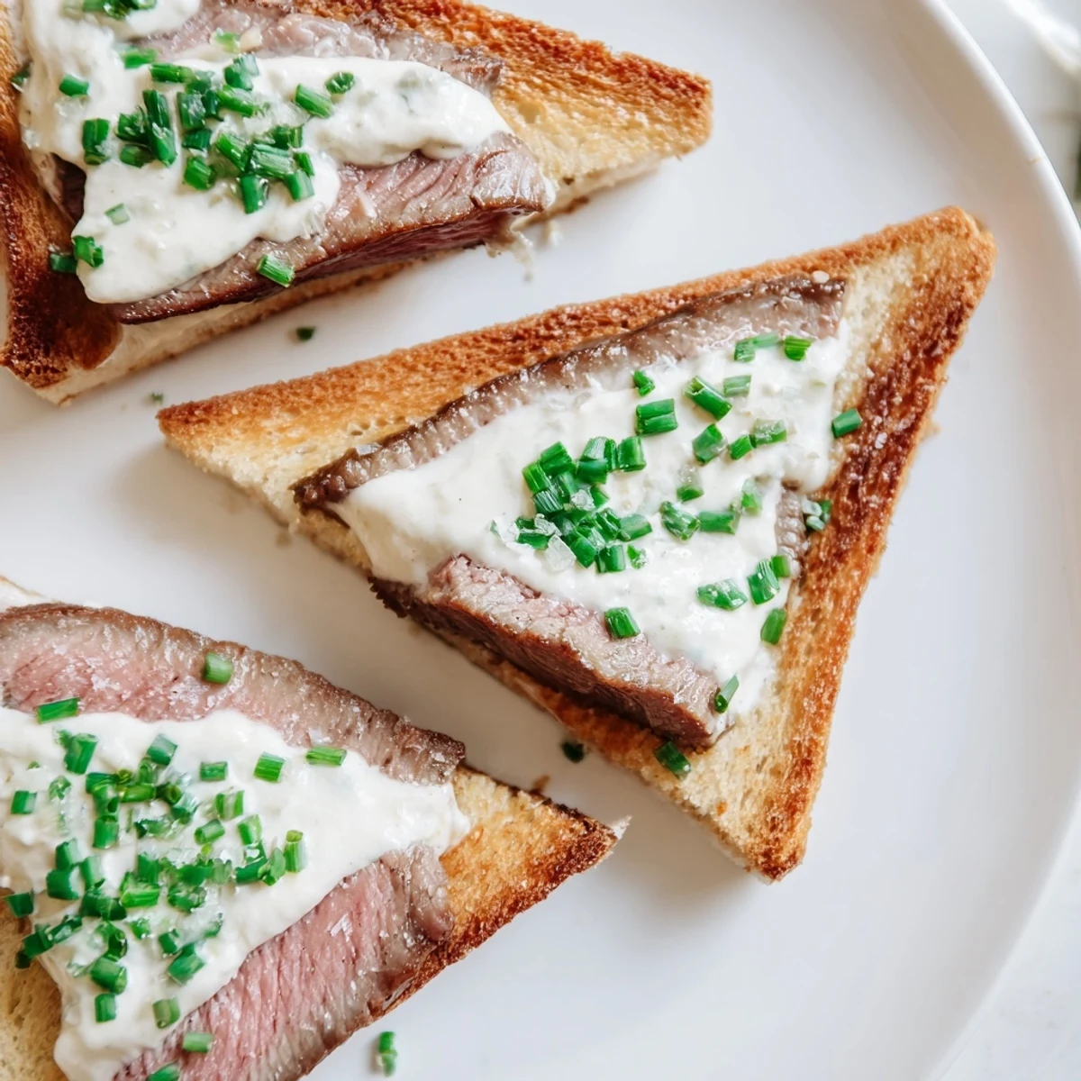 Freshly seared beef slices resting on warm buttery toast points drizzled with savory horseradish sauce.