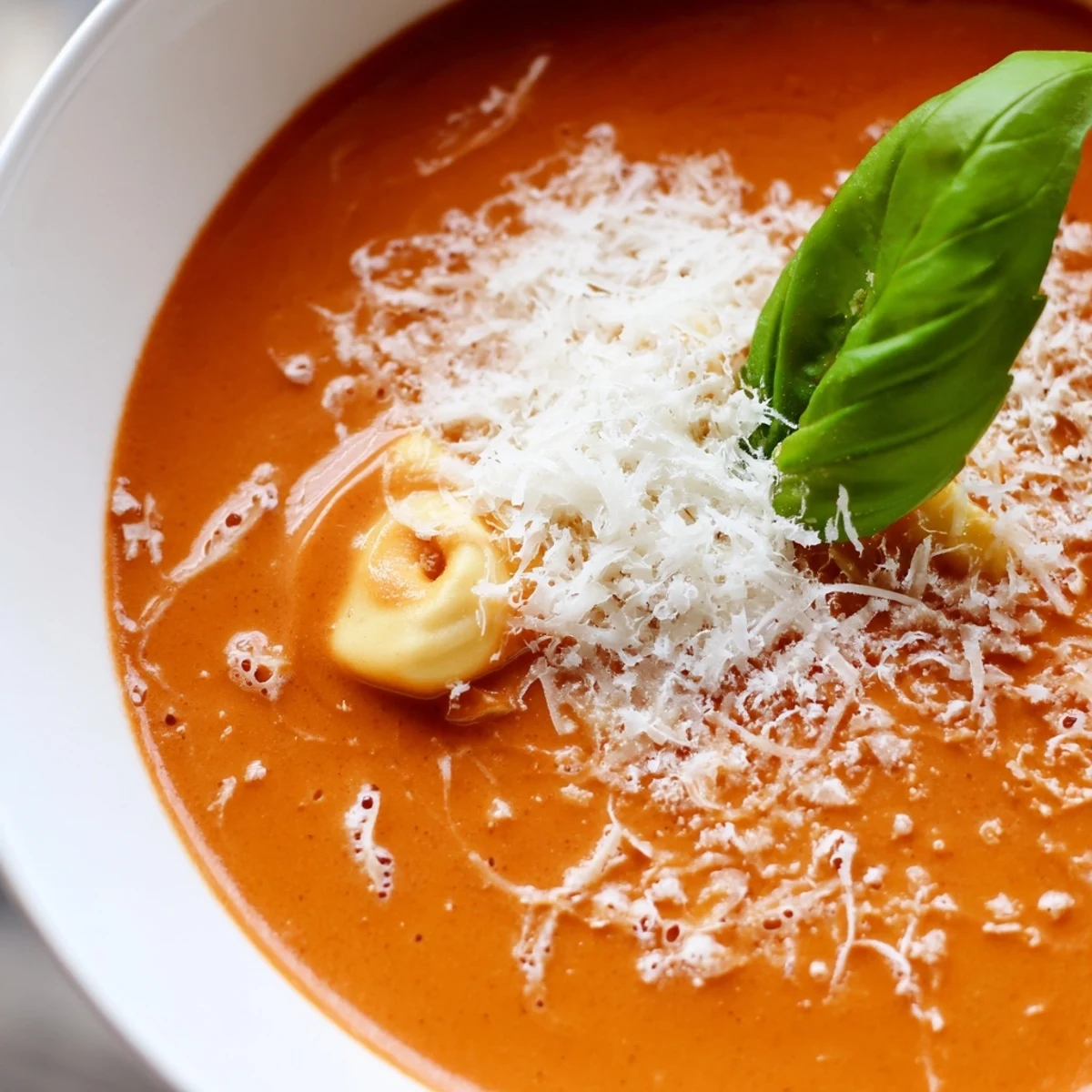 A pot of One Pot Creamy Tomato Tortellini Soup simmering with steam, fresh herbs, and a wooden ladle.