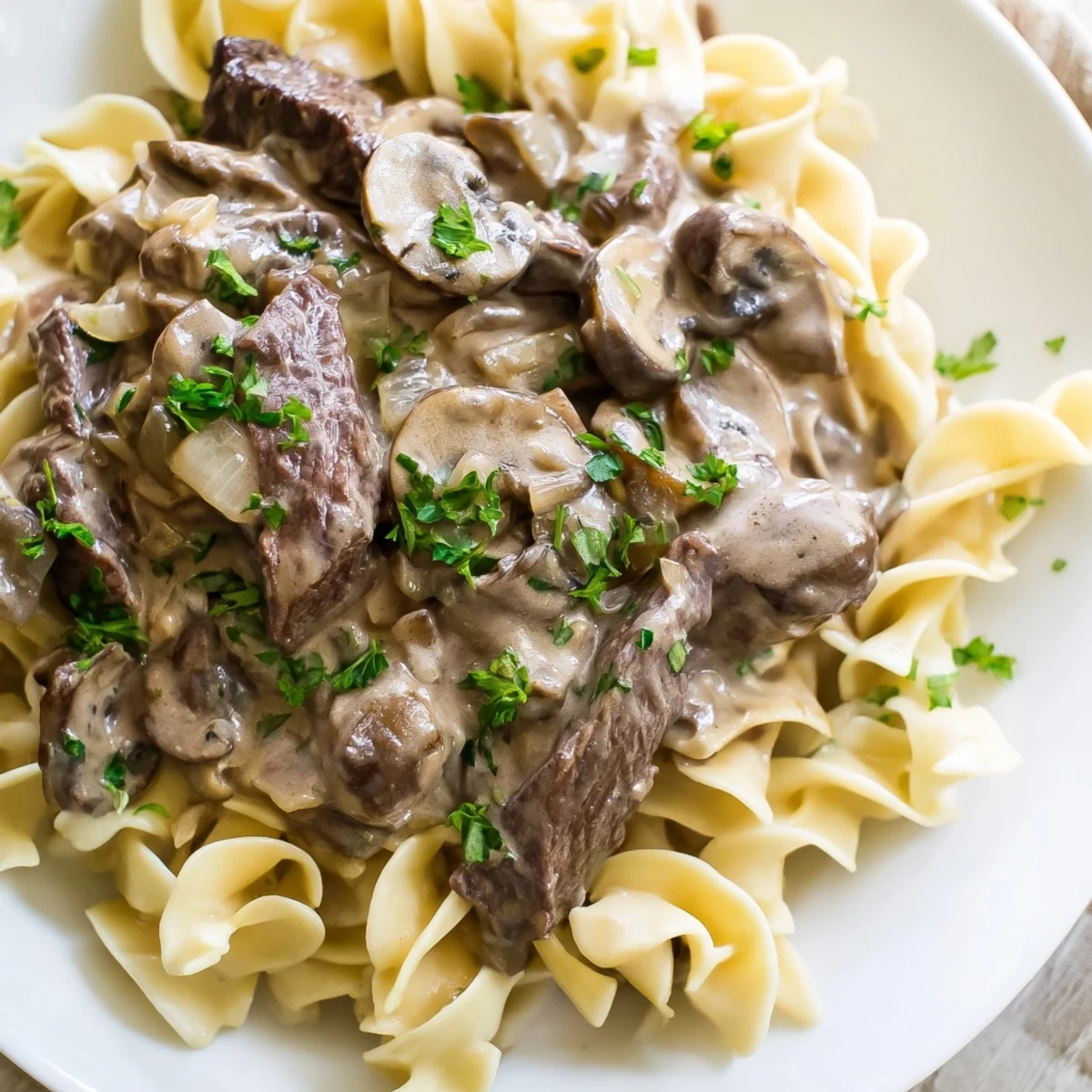 Savory Beef Stroganoff served over a bowl of buttery egg noodles, garnished with fresh parsley.