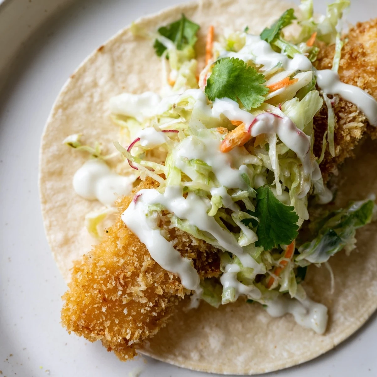 Crispy Fish Tacos with Cabbage Slaw piled high with golden fried cod, creamy sauce, and fresh lime wedges on a plate.