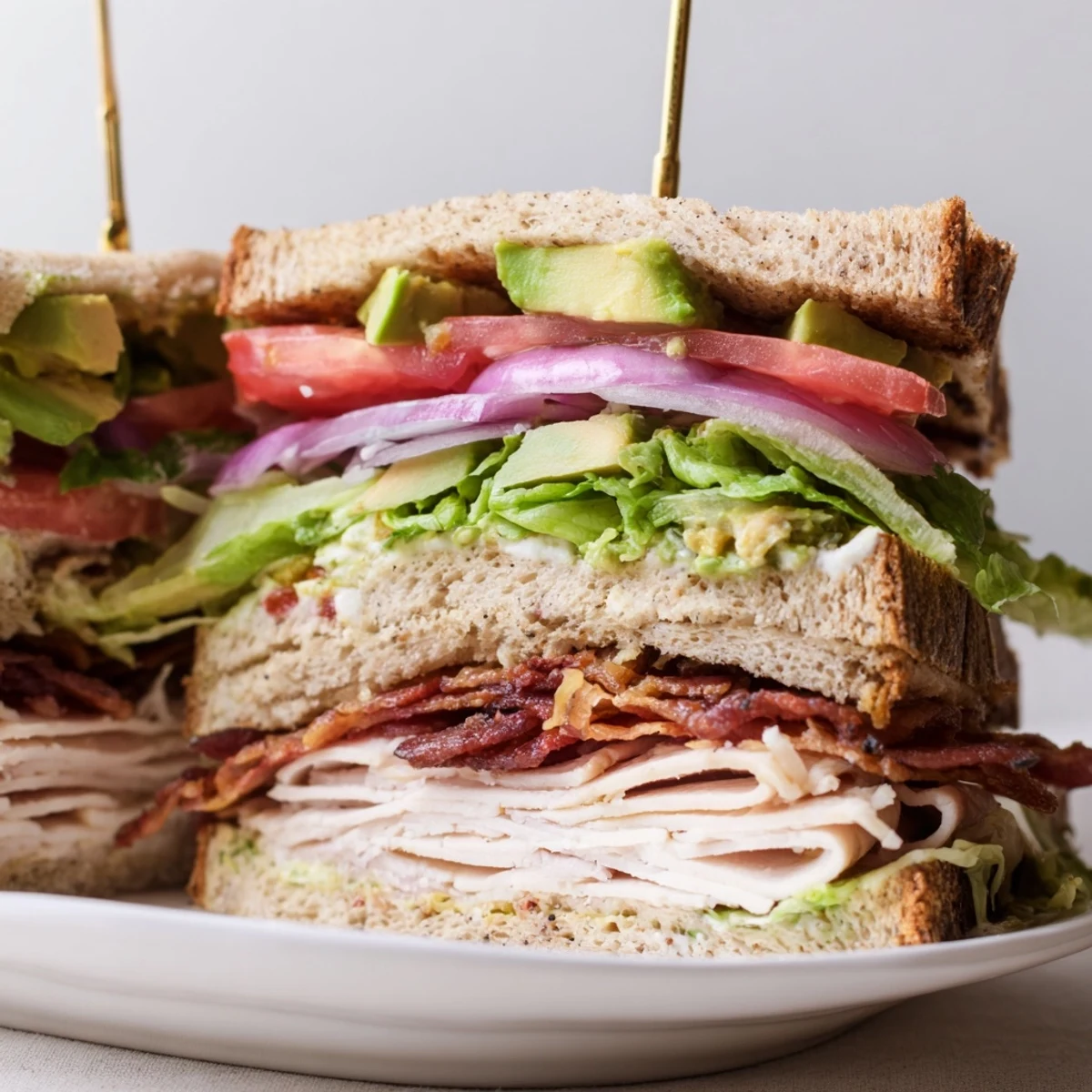 Freshly toasted bread layers a Turkey Club Sandwich with Turkey Bacon and Avocado, with creamy avocado and crispy bacon peeking out.
