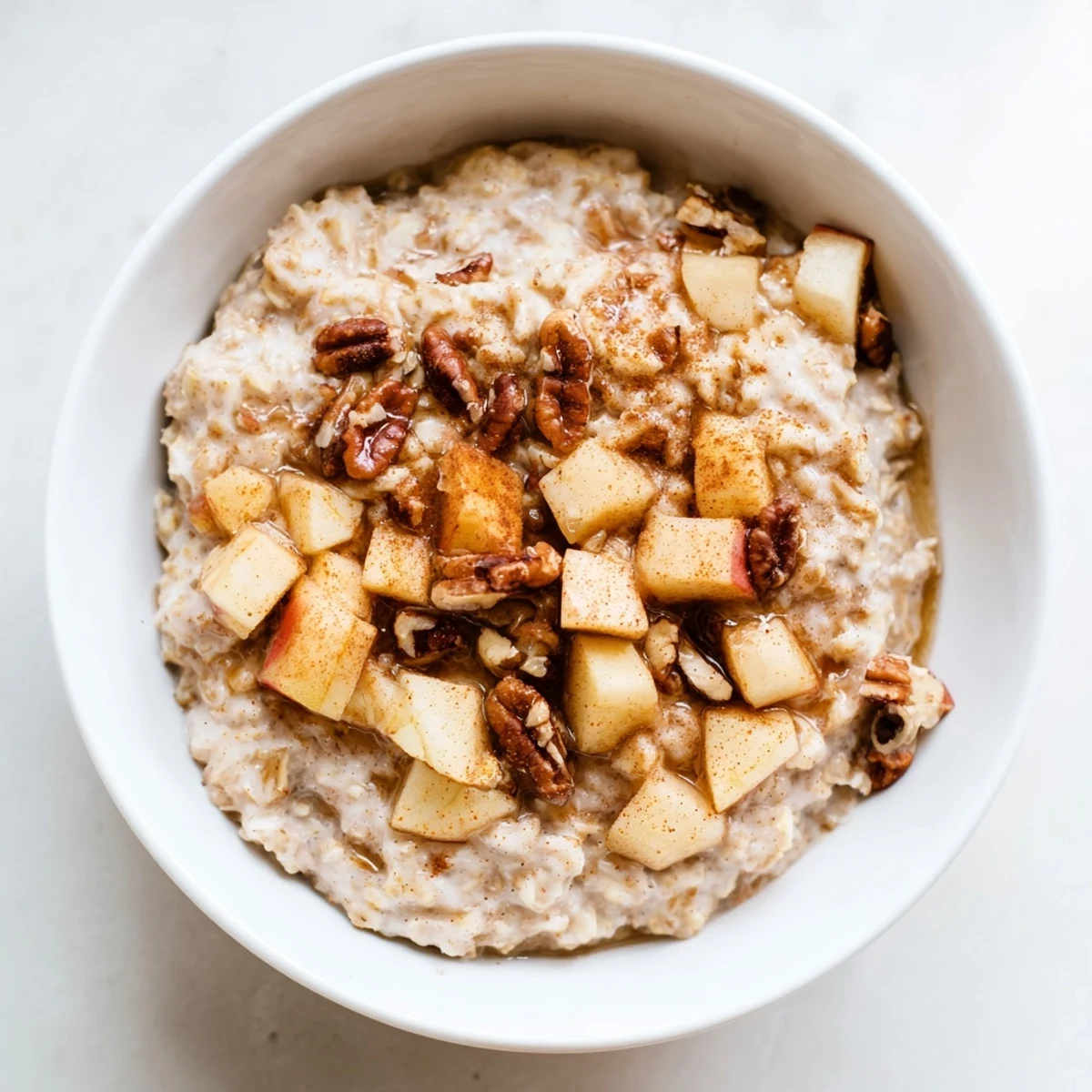A cozy morning breakfast of Warm Apple Cinnamon Oatmeal with Pecans, garnished with sliced apples and a drizzle of maple syrup.  