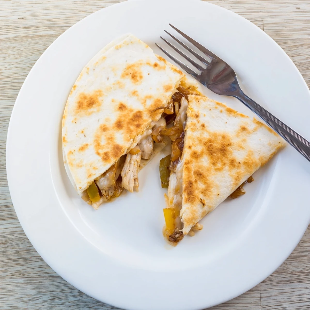 Overhead shot of Chicken Quesadillas with Peppers and Onions, paired with bowls of salsa and sour cream on a rustic table.