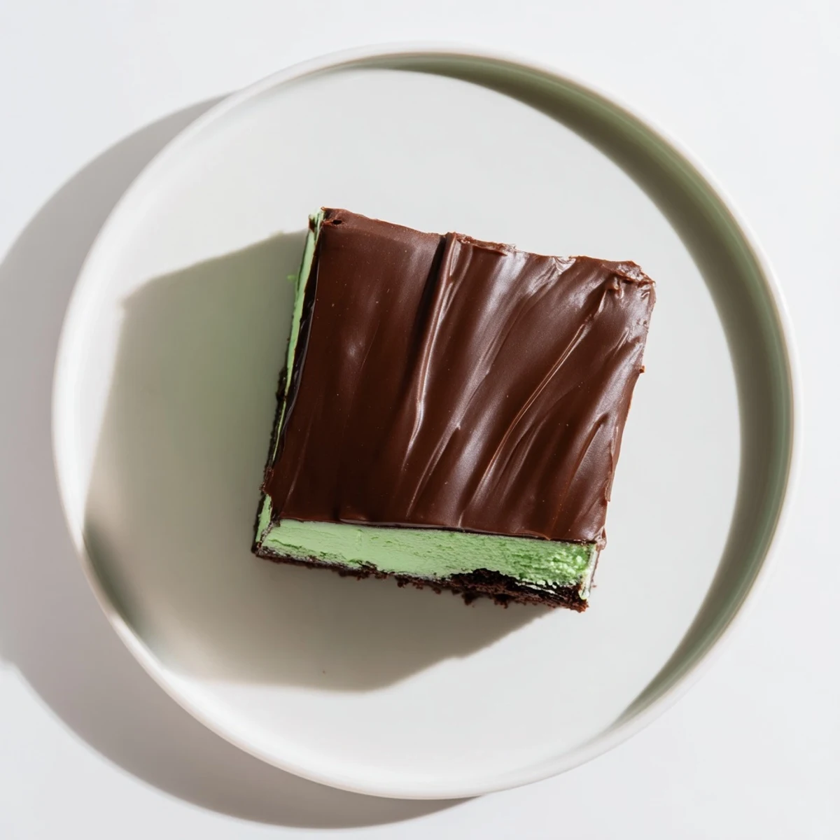 Freshly baked Green Mint Brownies with Ganache are arranged on a white plate, showcasing the moist brownie base and the cool mint filling.