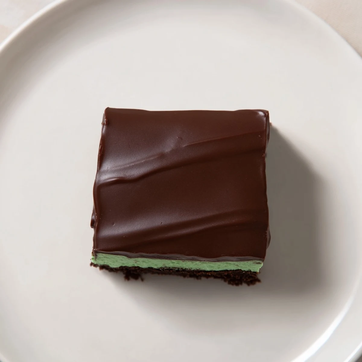 A close-up view of freshly cut Green Mint Brownies with Ganache, displaying a dark fudgy interior, mint green cream swirls, and glossy chocolate topping.