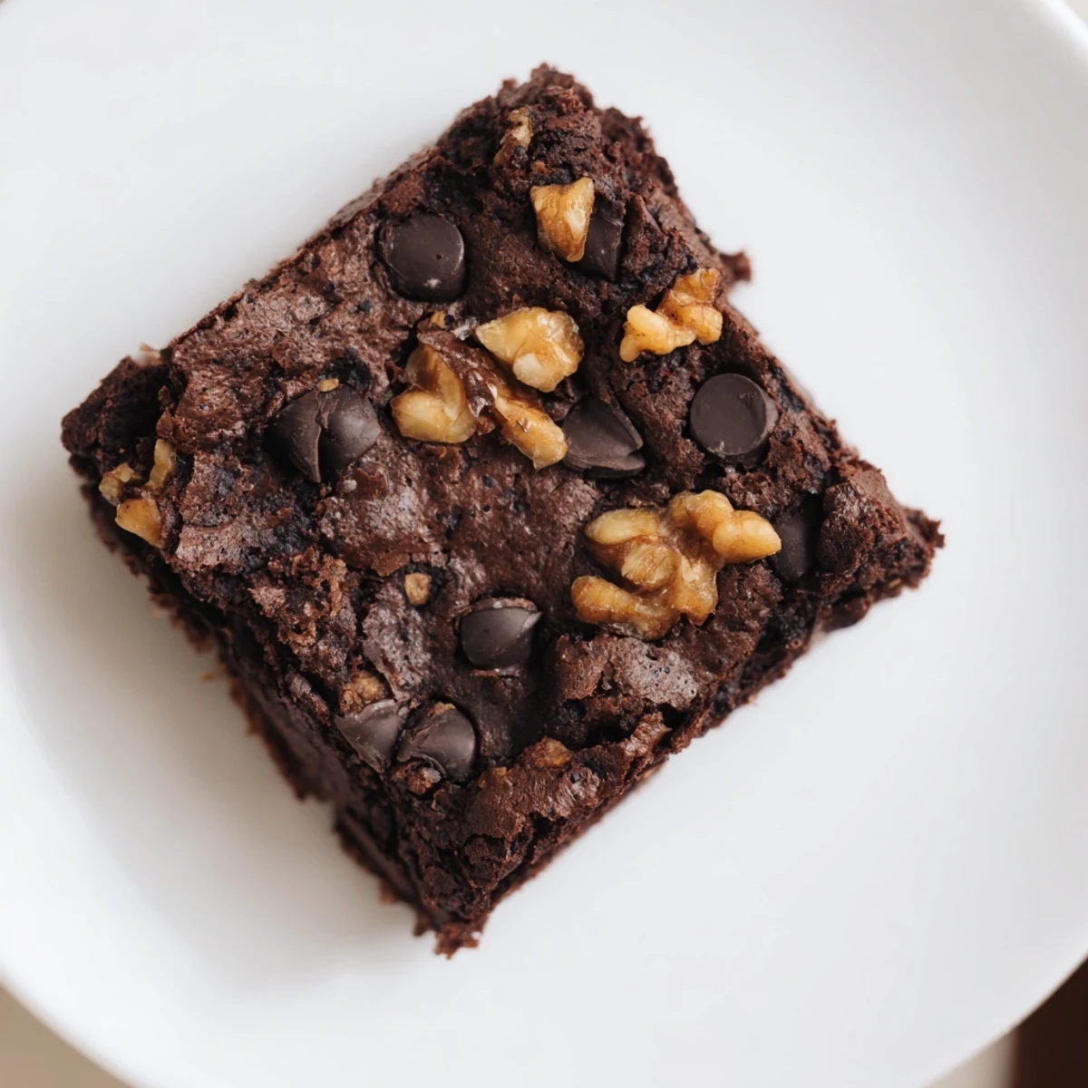 A close-up of freshly baked gluten-free almond flour brownies on a white plate, showcasing a rich, fudgy texture with glossy chocolate chips melted on top.