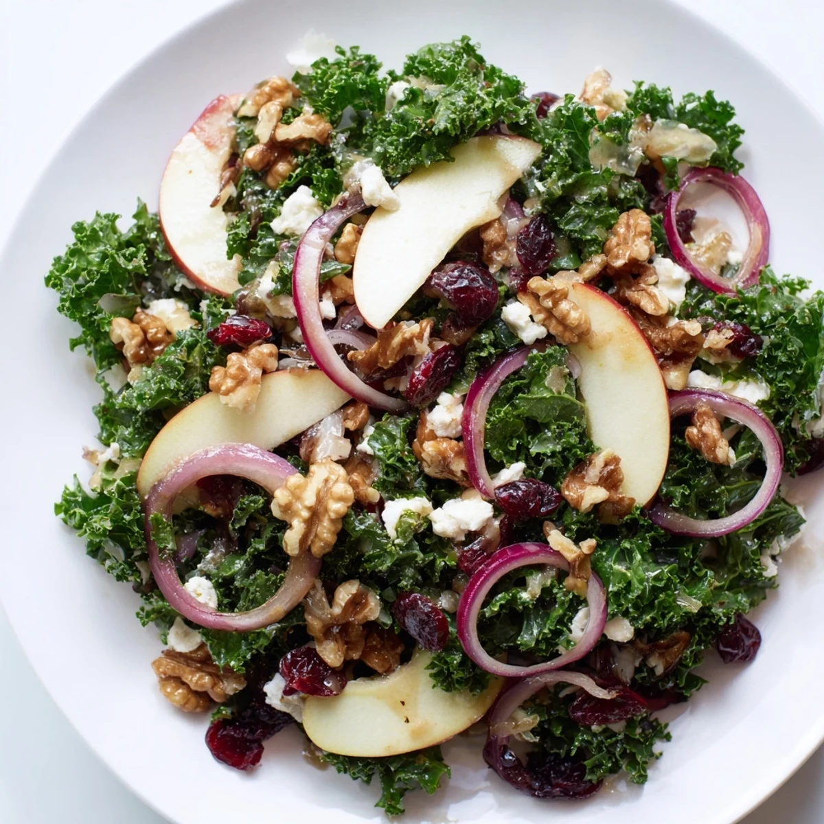 Fresh kale leaves are tossed with crisp apple slices, toasted walnuts, and a tangy maple-Dijon dressing in a large white bowl.
