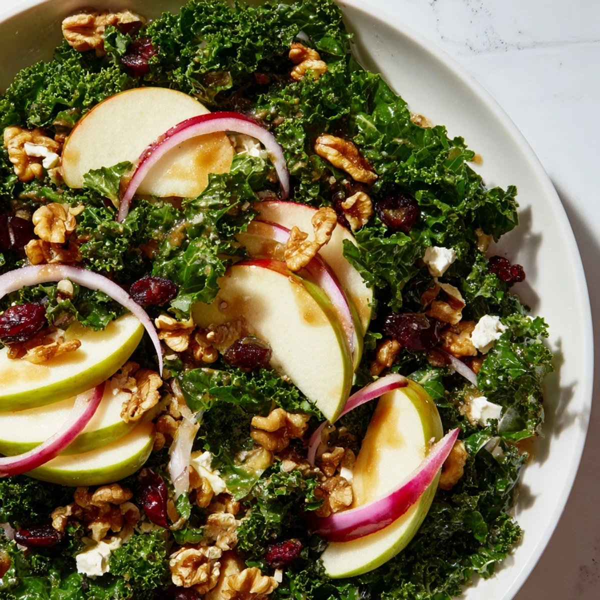 Green Kale and Apple Salad is topped with crumbled feta, dried cranberries, and thin red onion slices, served as a vibrant side.