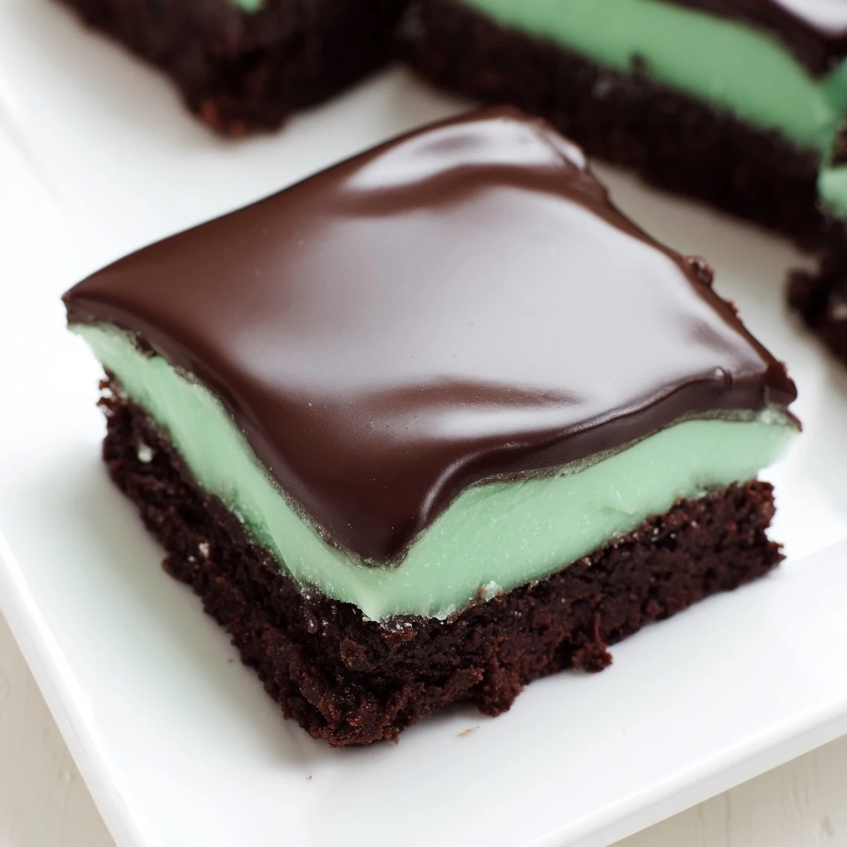 Square Shamrock Mint Brownies with Chocolate Ganache topped with glossy chocolate and fresh mint leaves.