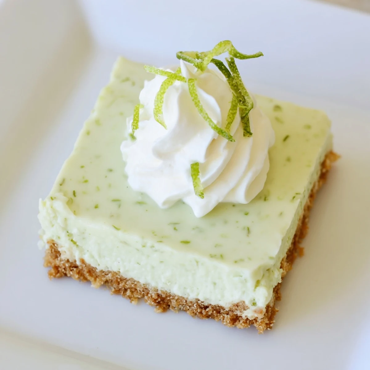 A single chilled Key Lime Pie Bar is served on a white plate with a lime wedge garnish for a refreshing dessert.