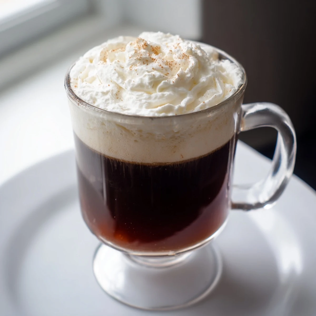 Close-up of Irish Coffee Mocktail with Whipped Cream featuring a fluffy cream swirl melting into hot coffee.