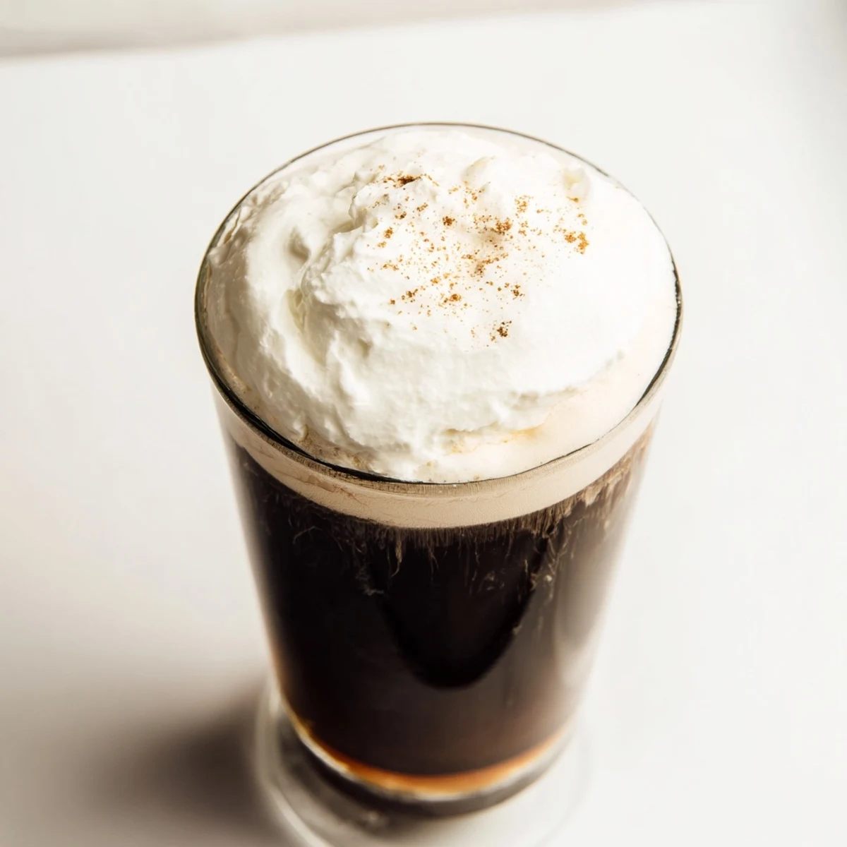 The Irish Coffee Mocktail with Whipped Cream shows layered textures, glossy brown coffee beneath soft white peaks, garnished simply for a cozy feel.