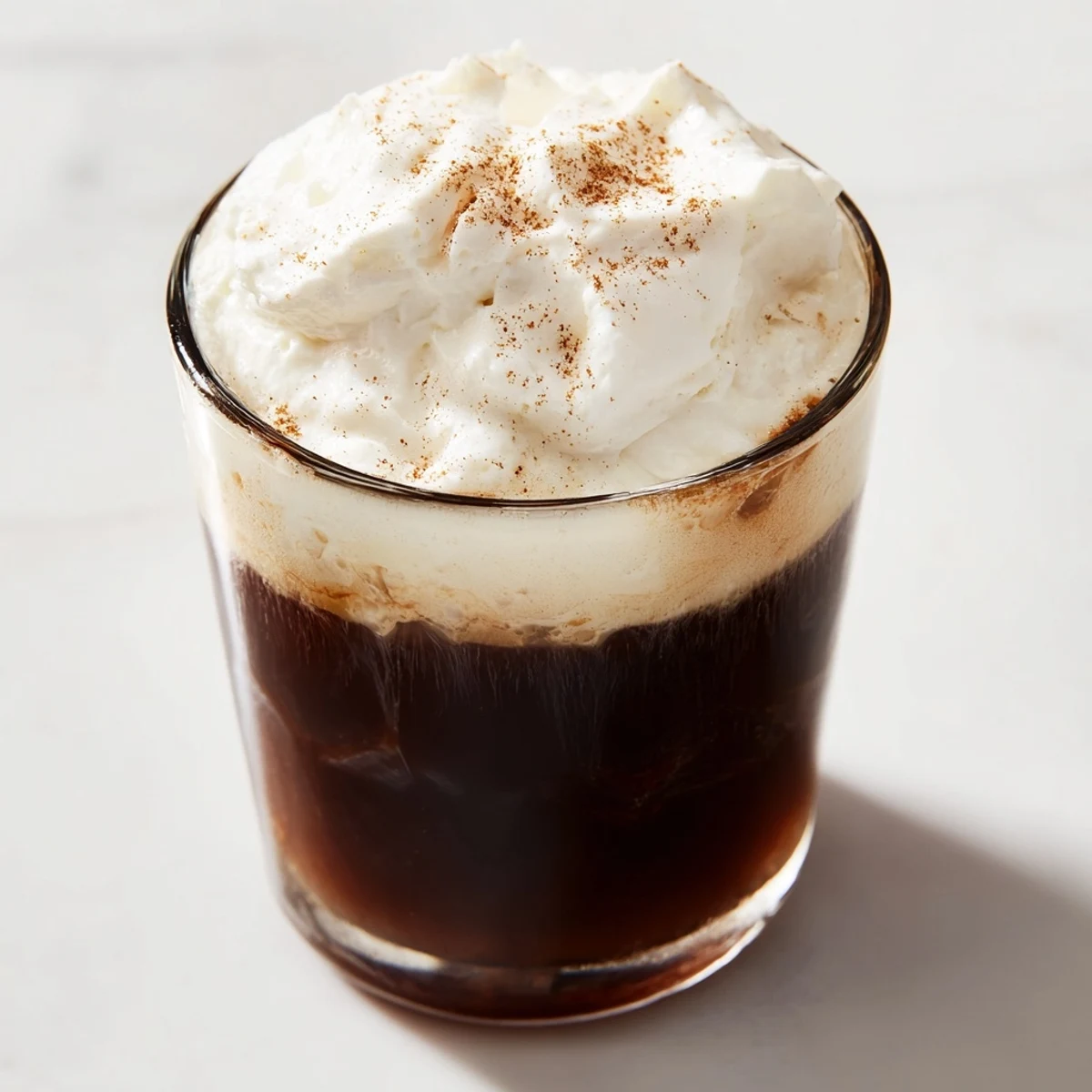 Steaming Irish Coffee Mocktail with Whipped Cream in a clear glass mug, topped with a thick cloud of cream and nutmeg dusting.