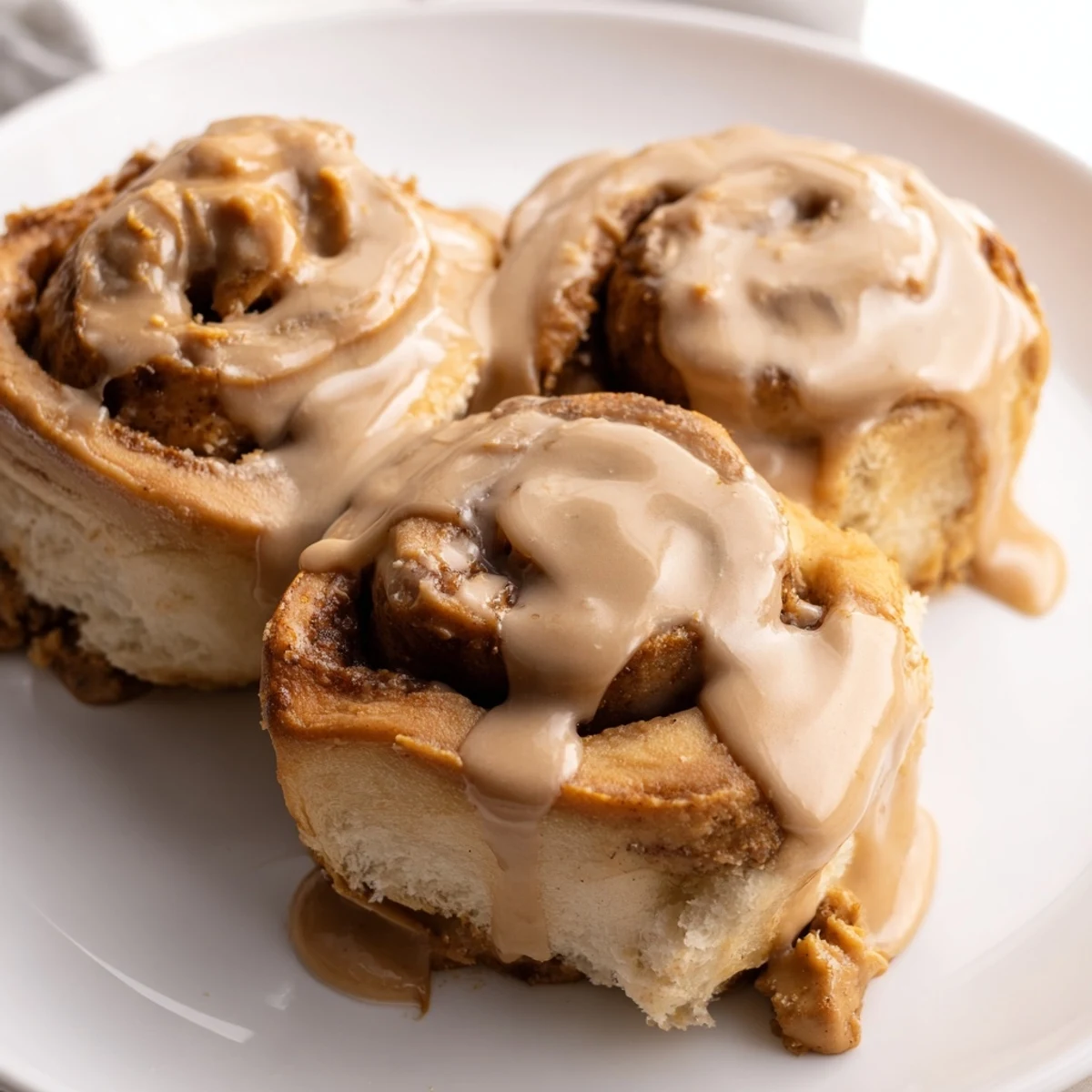 Close-up view of Soft and Gooey Biscoff Cinnamon Rolls on a white plate, showing melted Biscoff spread and cinnamon sugar filling.