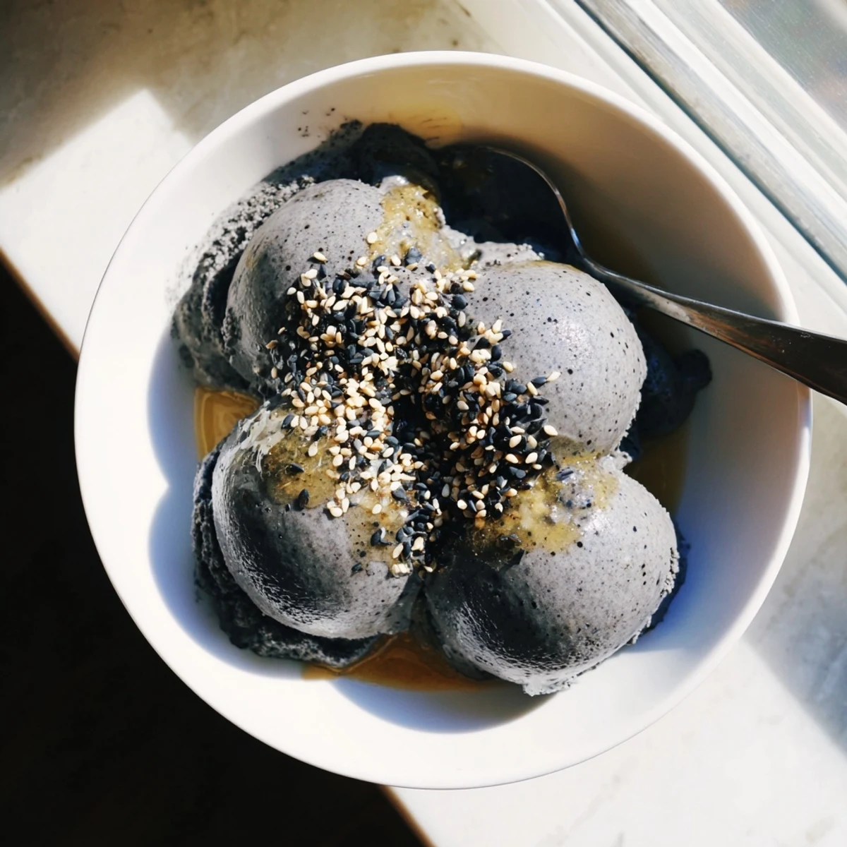 A close-up of the Toasted Black Sesame Ice Cream reveals its smooth texture and speckled seed bits in a chilled bowl.