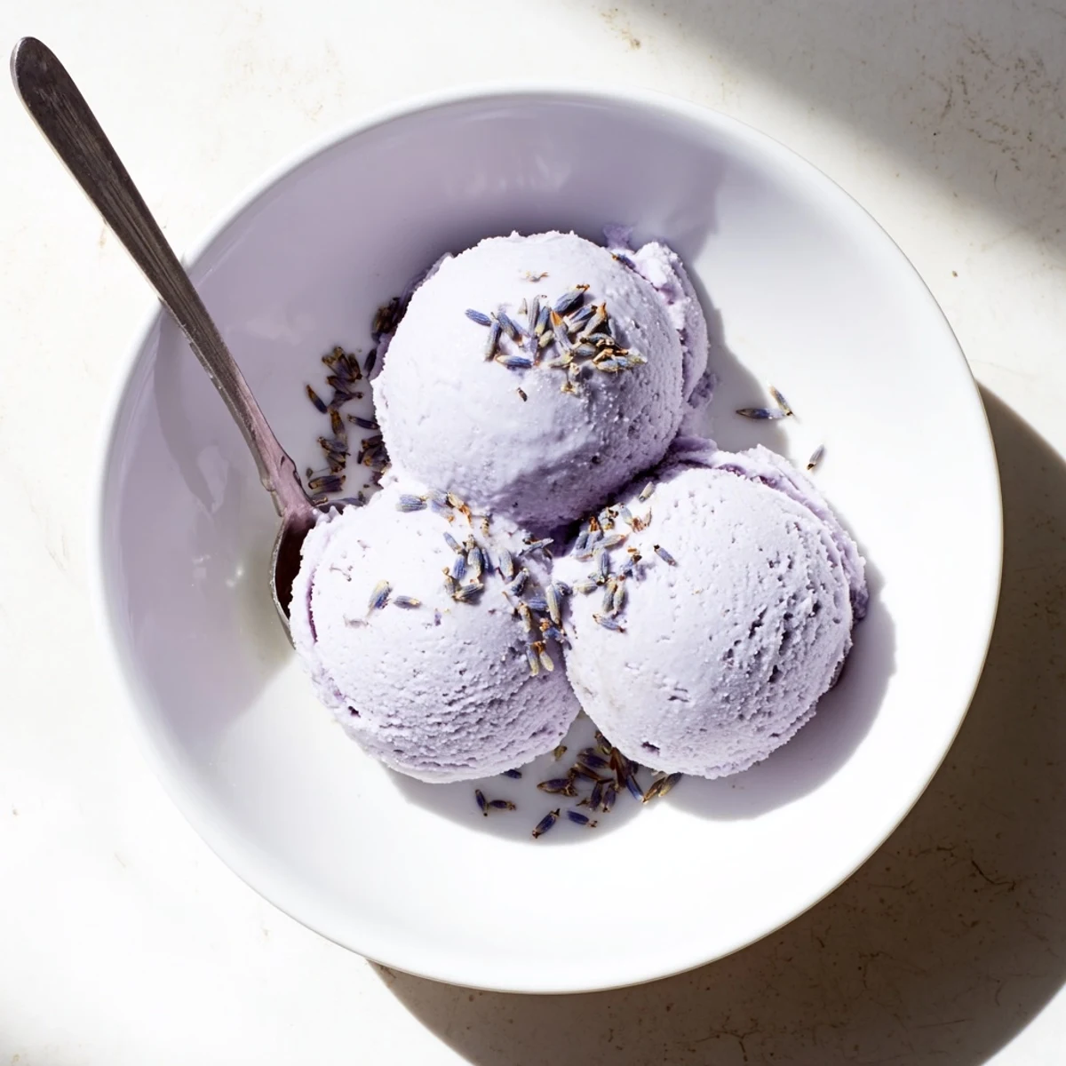 Creamy lavender ice cream scoops glisten in a bowl beside fresh berries and shortbread.