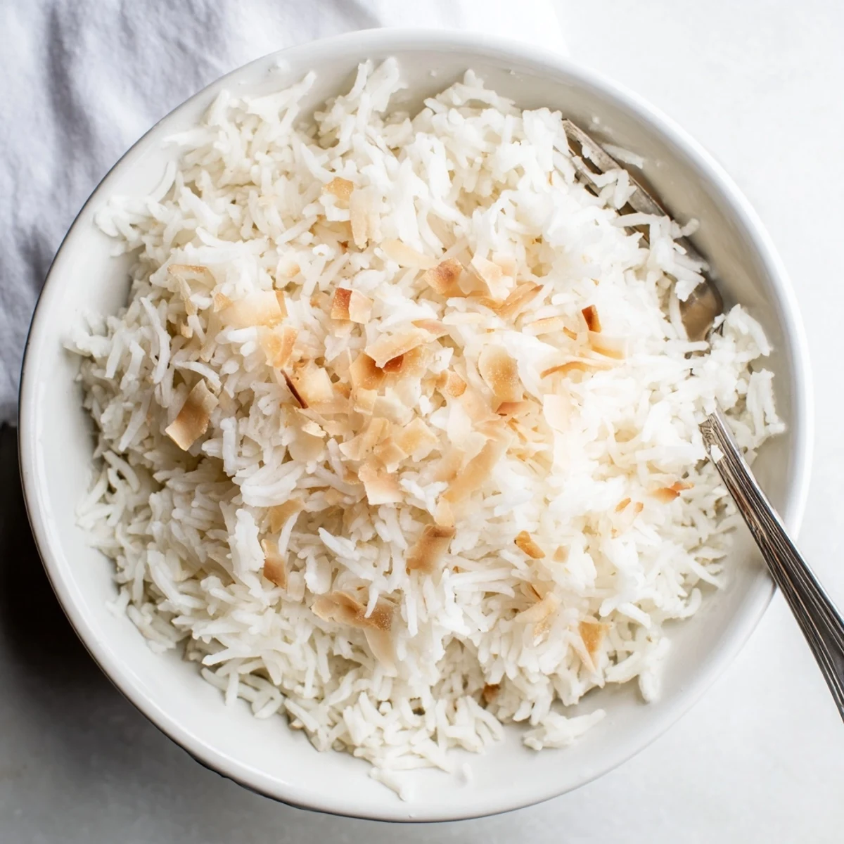 A fork lifts tender portions of The Best Coconut Rice, revealing its subtle sweetness and aromatic texture beside grilled chicken.