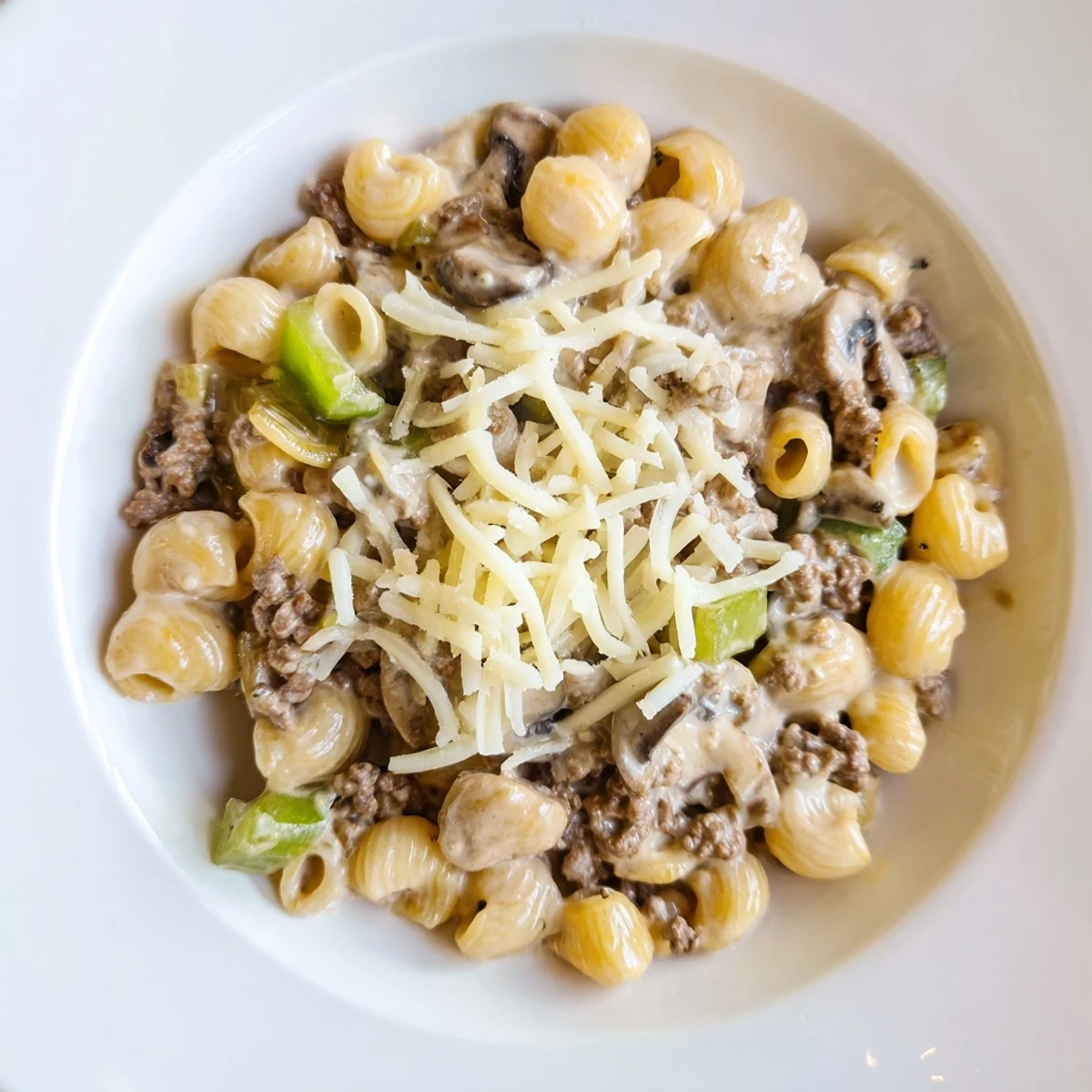 Steaming bowl of Easy High Protein Philly Cheesesteak Mac topped with melted provolone and chopped parsley.