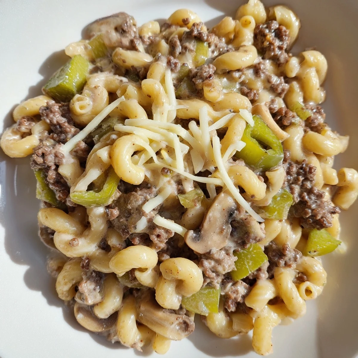 Fork lifting a cheesy serving of Easy High Protein Philly Cheesesteak Mac with sautéed peppers and onions.