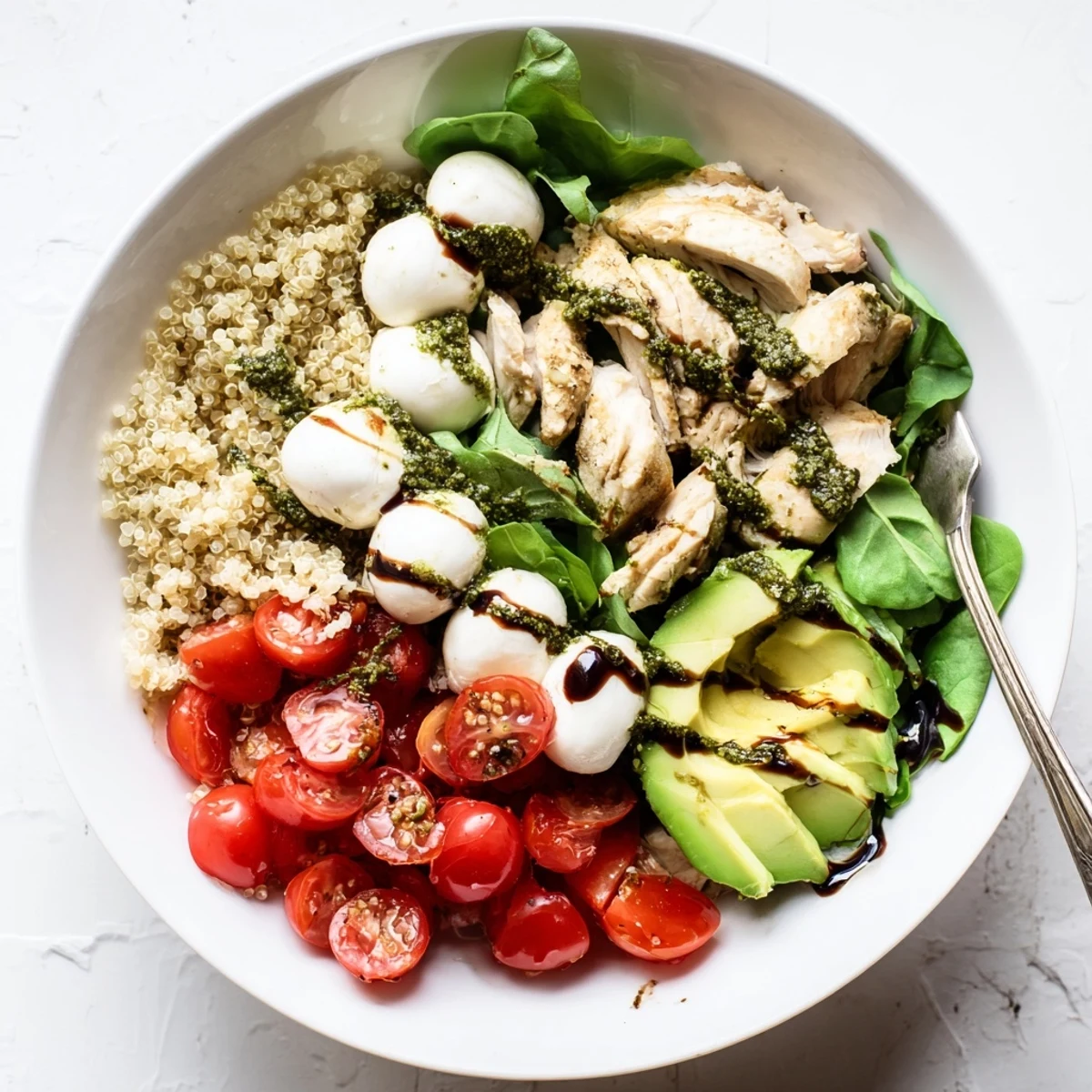 A vibrant Pesto Chicken Caprese Grain Bowl features torn basil leaves, baby spinach, and mozzarella, prepared with grilled chicken and colorful vegetables for a wholesome gluten-free dinner.