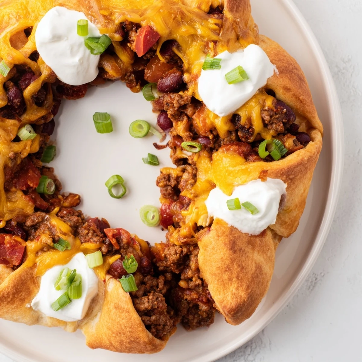 Family-style Beef Chili Taco Crescent Roll Ring rests on a rustic platter, golden crescents hugging hearty chili and shredded cheddar cheese.