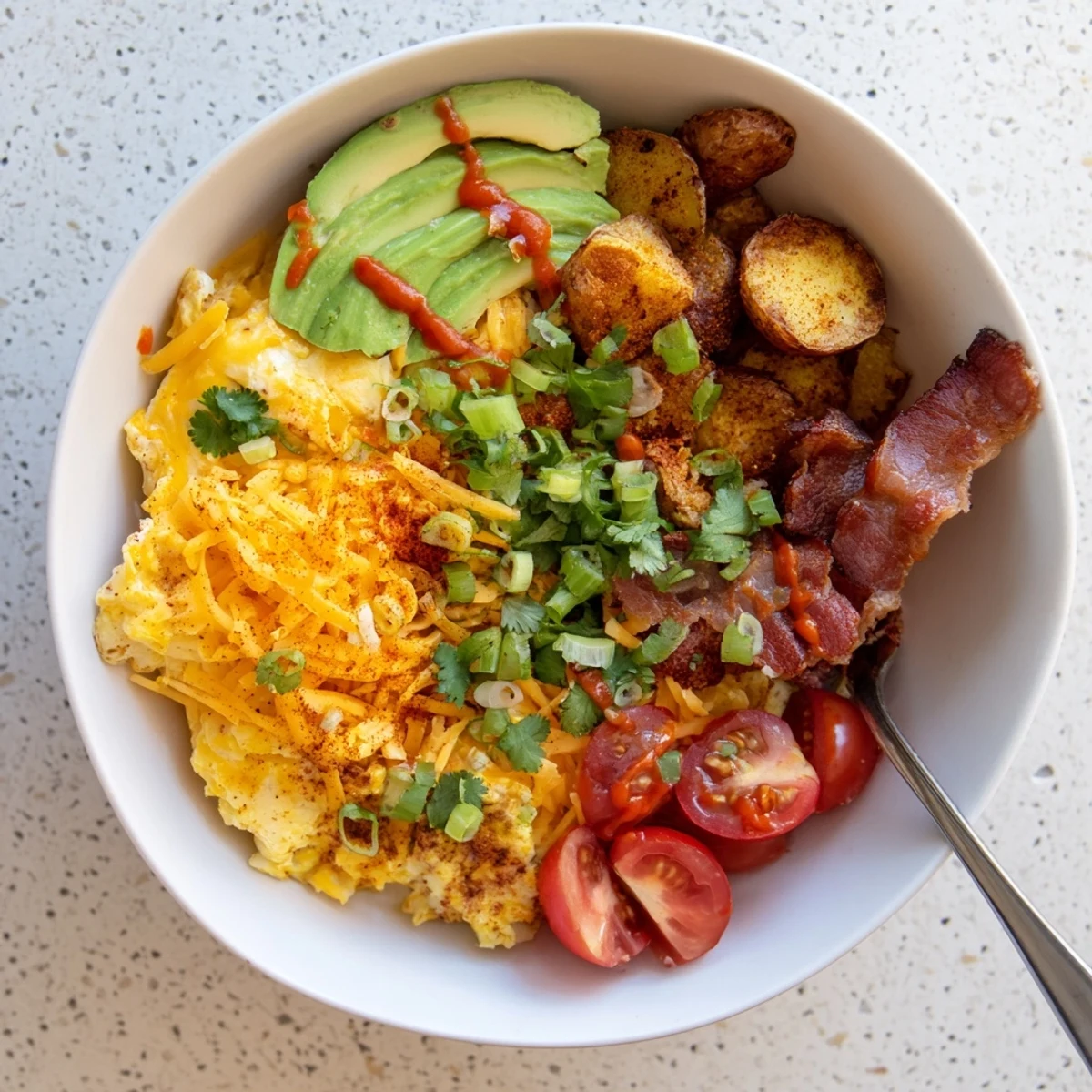 The Loaded Breakfast Bowl showcases diced avocado, cherry tomatoes, and green onions adding vibrant color and fresh flavor to the hearty meal.