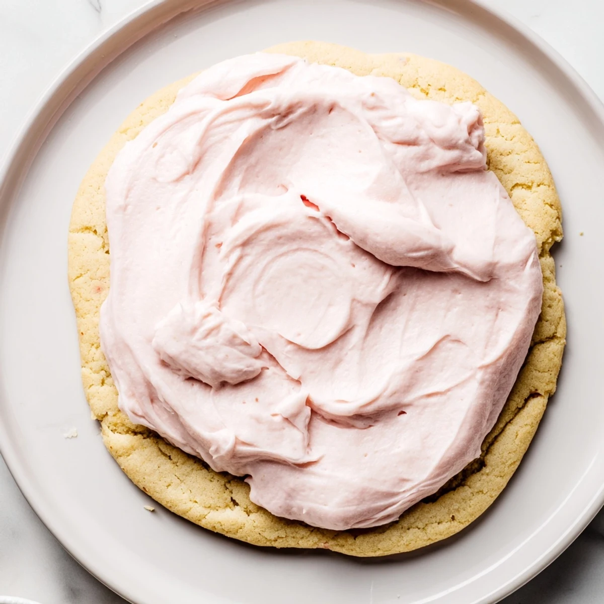 A close-up of a giant Crumbl sugar cookie with pink frosting, ready to serve.