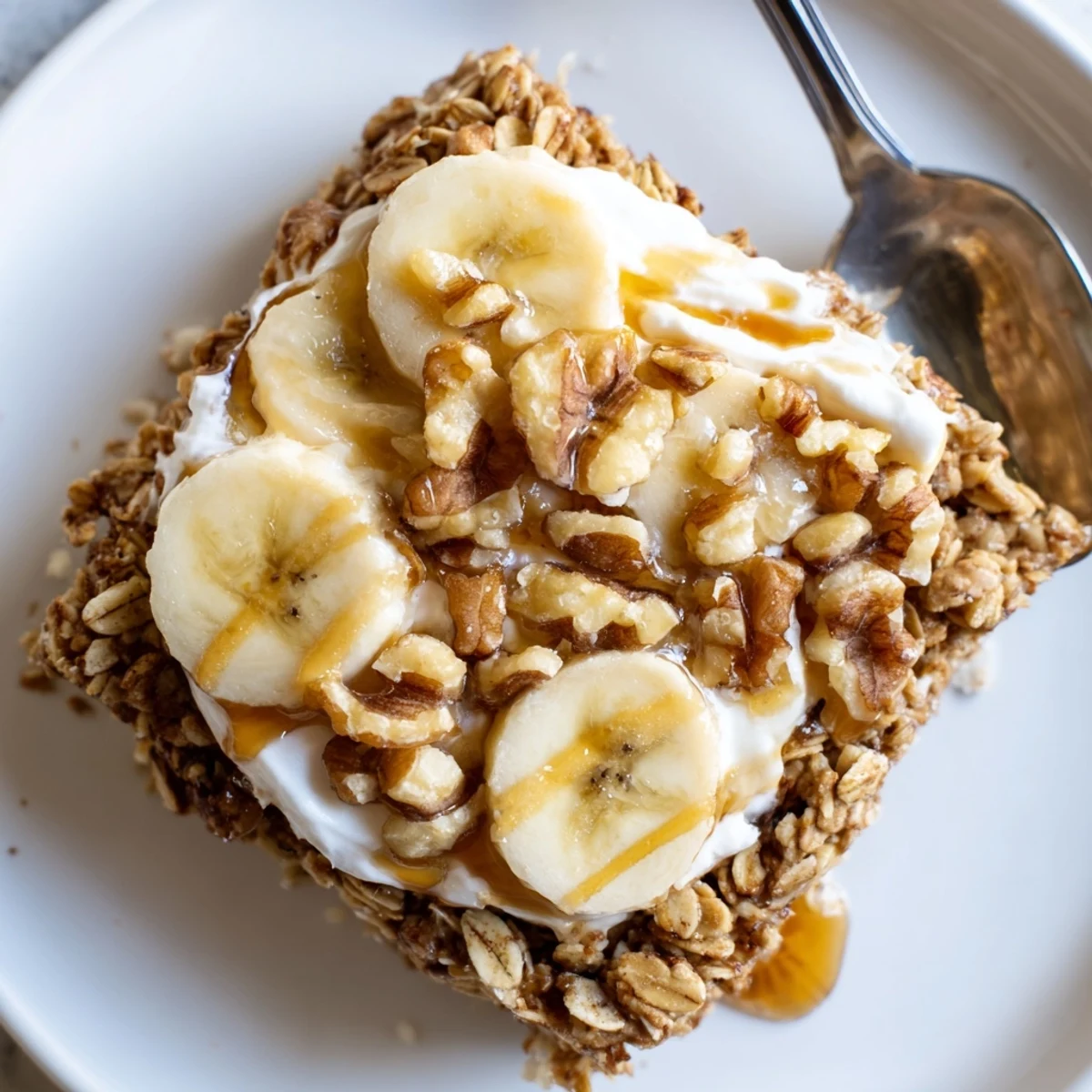 A warm slice of Banana Baked Oatmeal with Greek Yogurt, topped with fresh banana slices and a drizzle of honey for a cozy American breakfast.