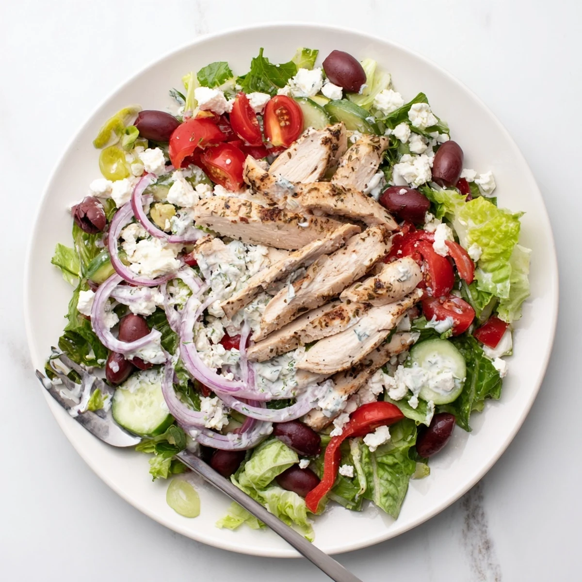 Sliced grilled chicken breast sits atop mixed greens, drizzled with creamy Tzatziki Chicken Salad dressing and garnished with feta.