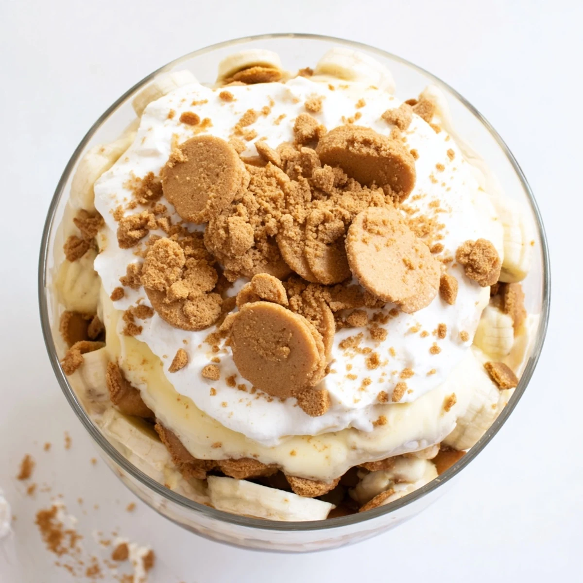 Glass trifle dish showcasing Biscoff banana pudding with layered fresh bananas, spiced cookies, and fluffy whipped cream topping