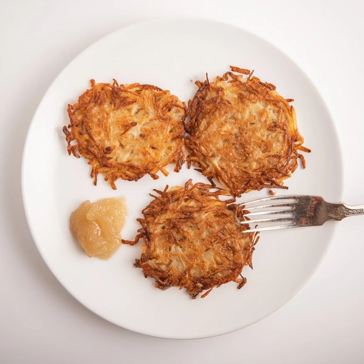 Golden brown German potato pancakes stacked on a white plate with dollops of sour cream and applesauce