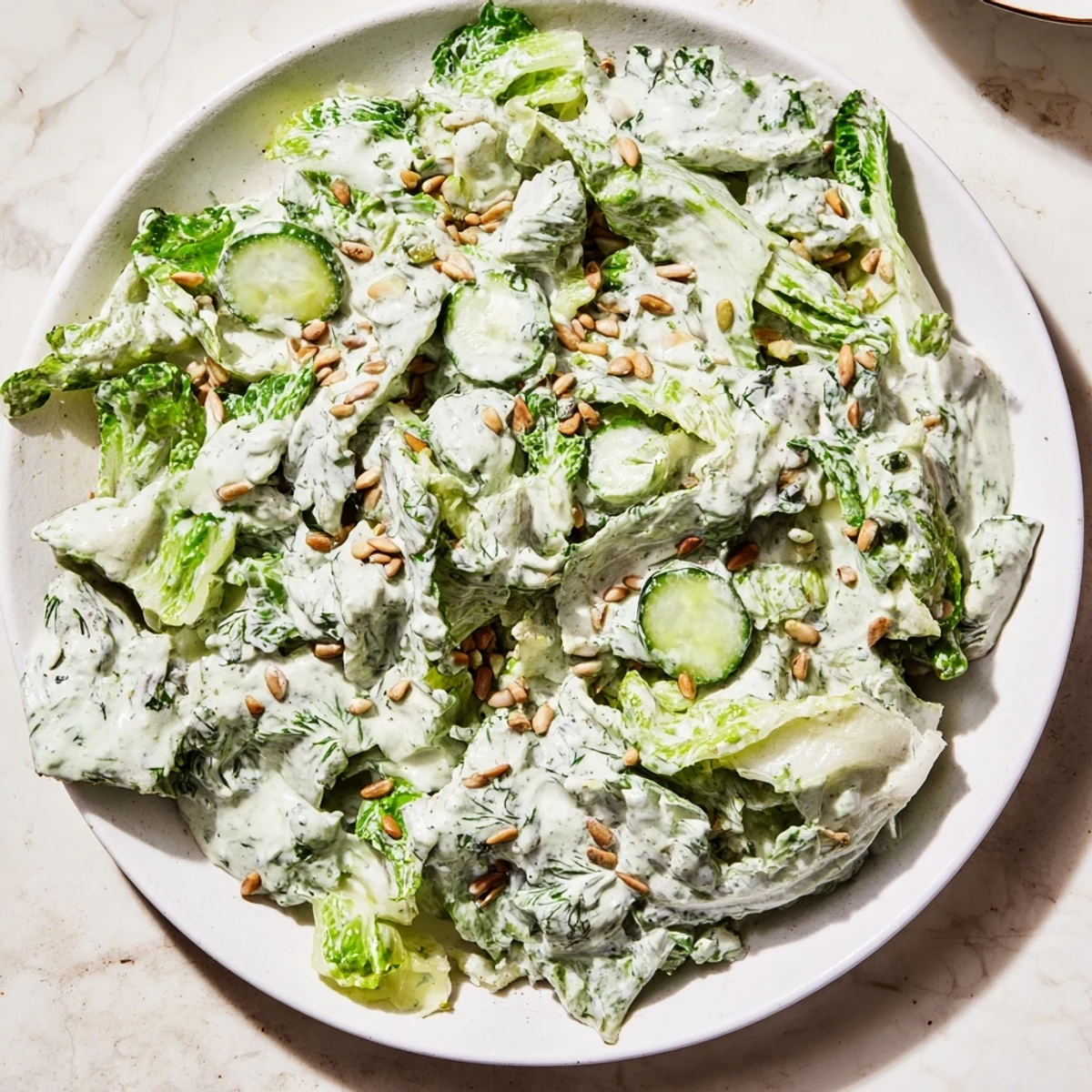 Colorful Green Goddess salad in white bowl with mixed greens, aromatic herbs, and creamy dressing garnished with seeds