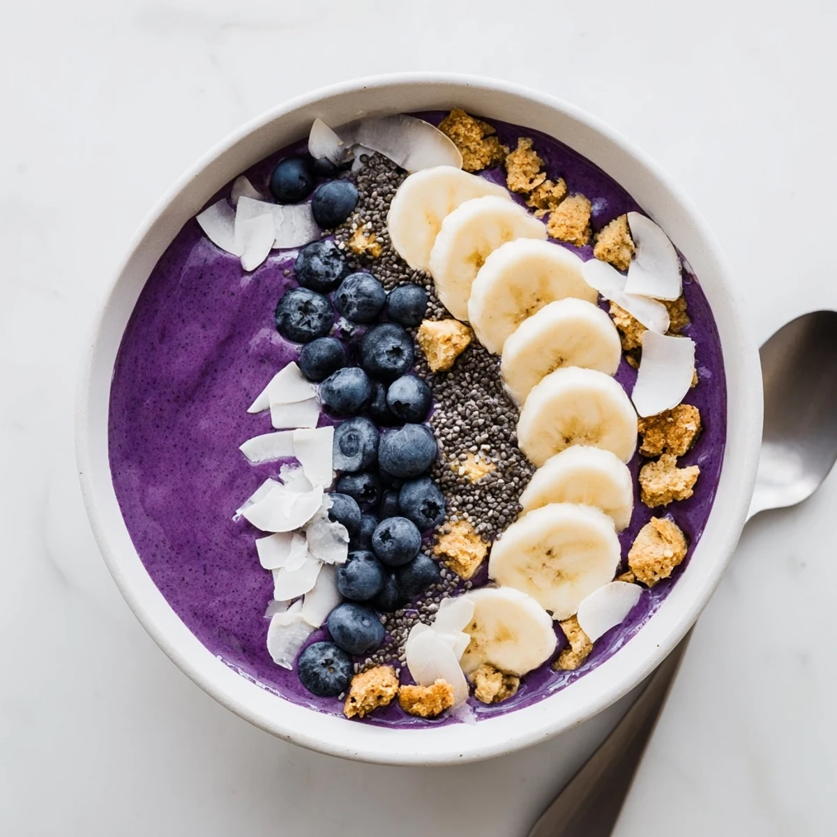 Thick blueberry smoothie bowl with Greek yogurt topped with fresh berries, granola, coconut flakes and sliced almonds