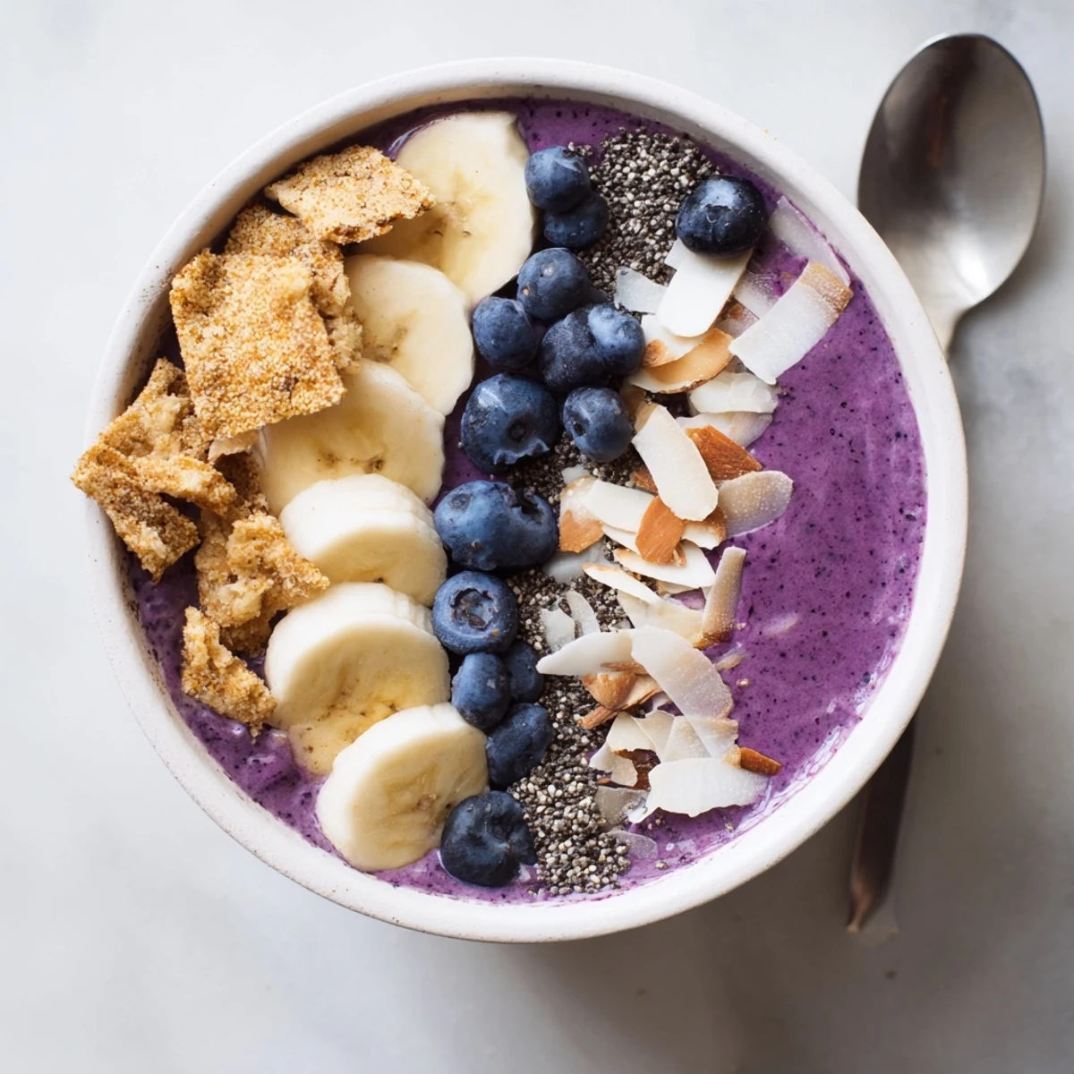 Creamy Greek yogurt blueberry smoothie bowl arranged with banana slices, chia seeds and crunchy almond toppings