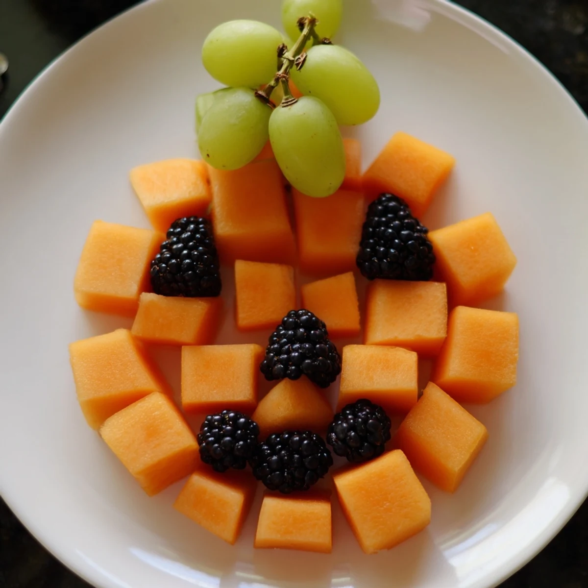 Healthy Halloween pumpkin fruit tray platter featuring fresh melon, berries, and green grapes