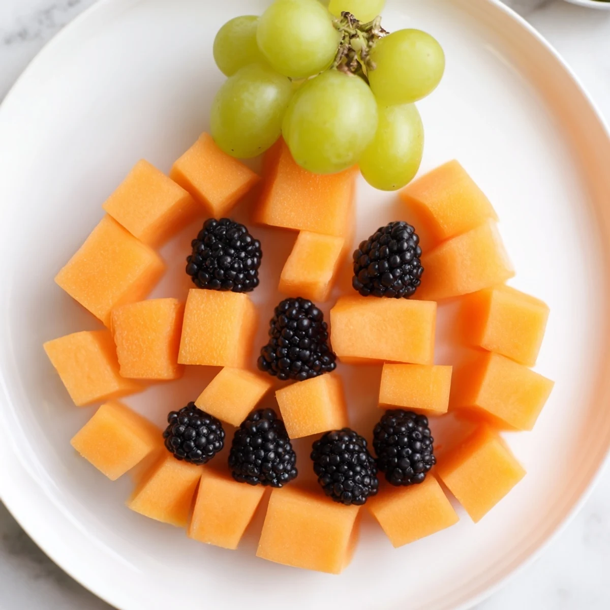 Vibrant pumpkin-shaped fruit tray Halloween platter with colorful cantaloupe, strawberries, and fresh mint