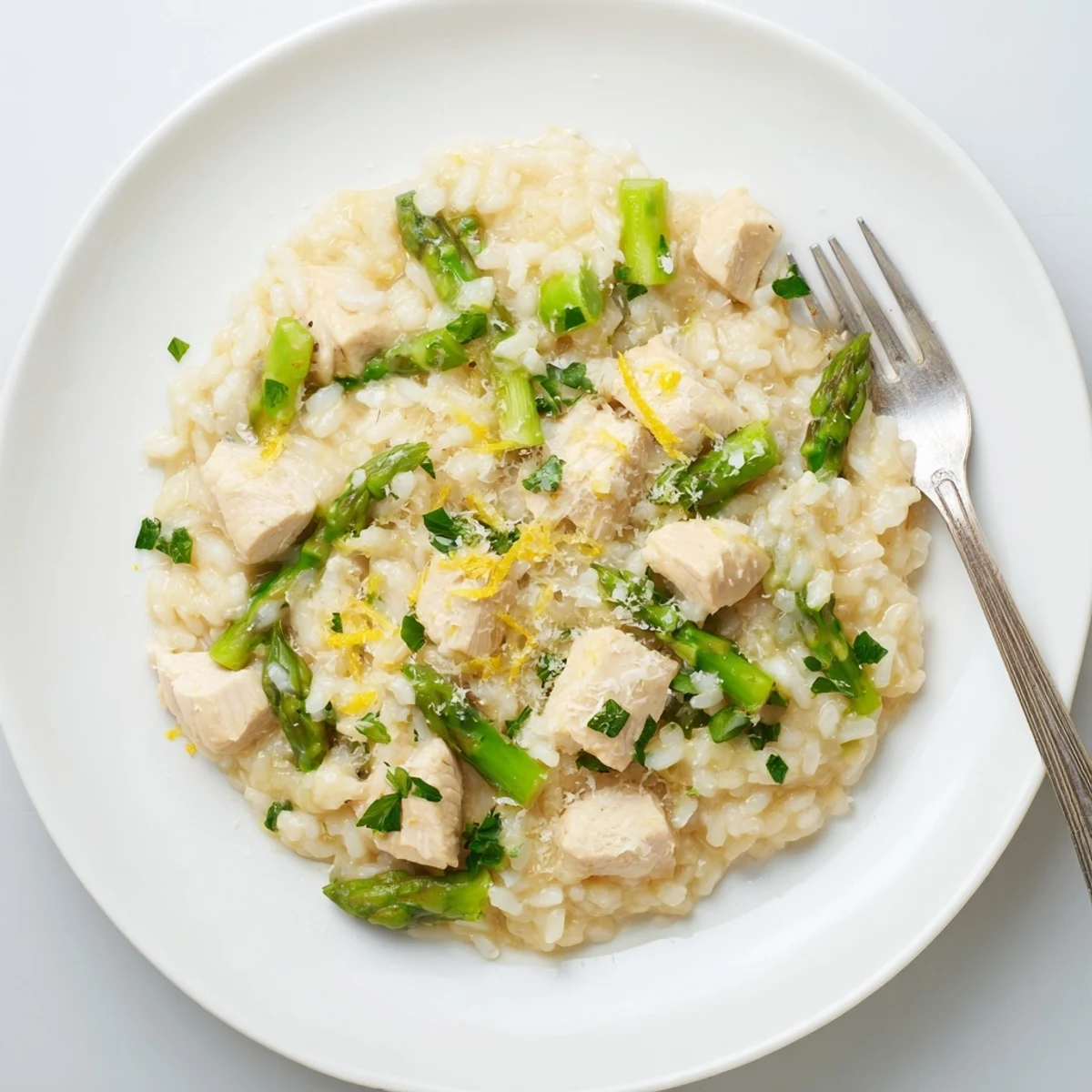 Steaming bowl of chicken and asparagus risotto garnished with lemon zest and extra cheese