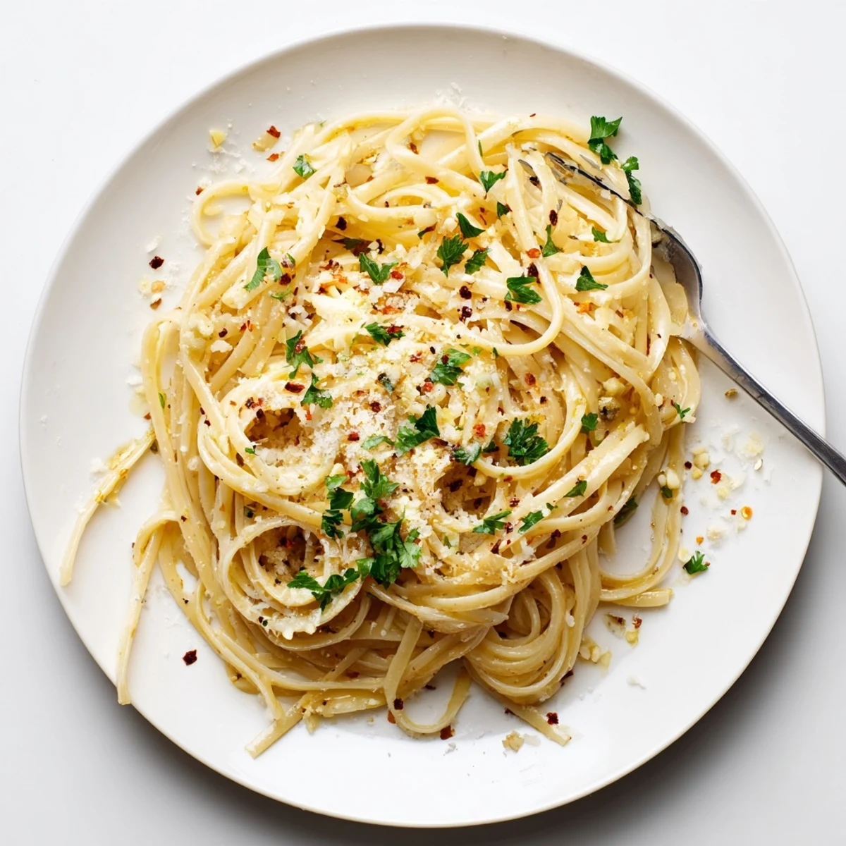 Golden strands of garlic butter pasta twirled on a white plate topped with fresh parsley and grated Parmesan cheese.