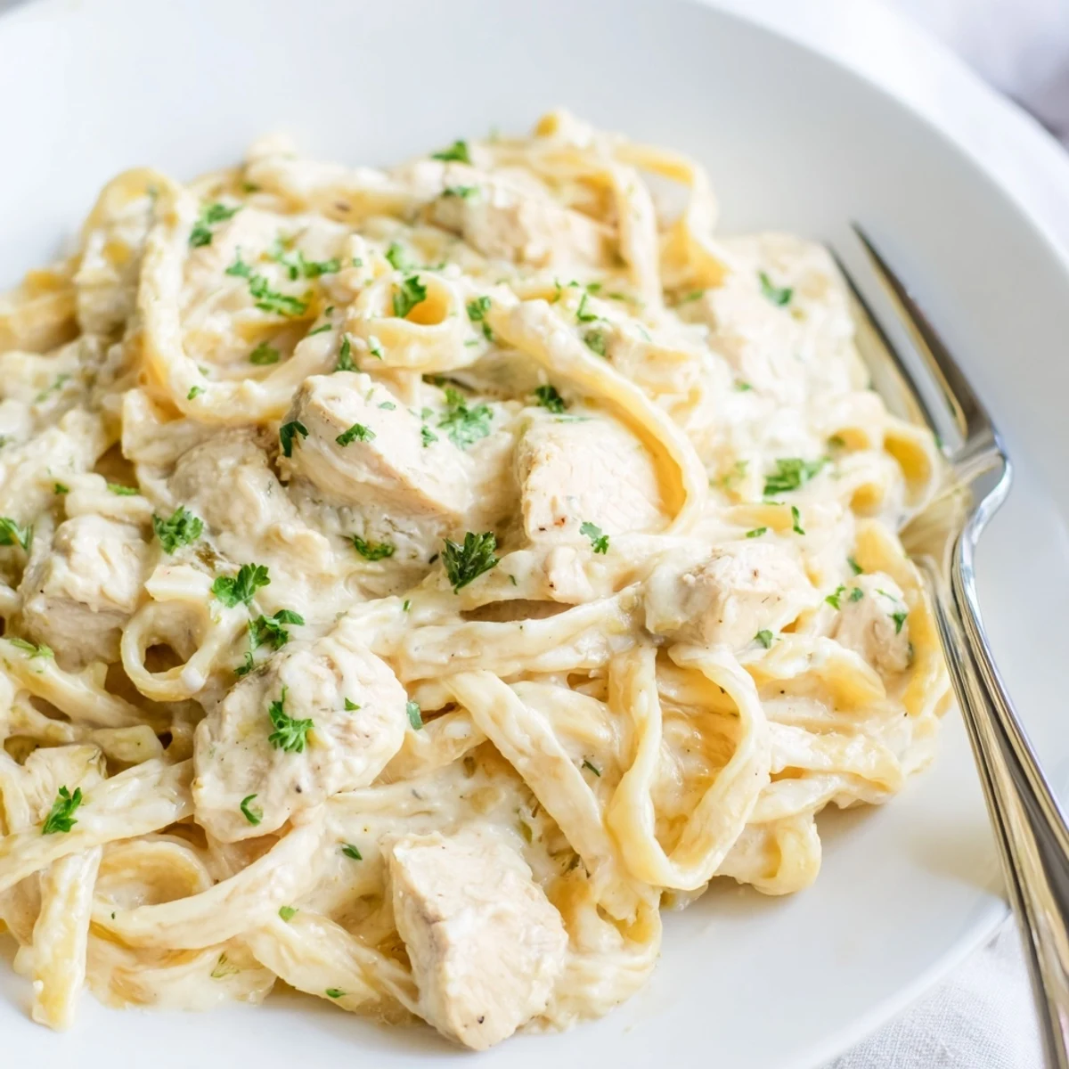 Golden chicken breast pieces nestled among fettuccine noodles in a thick white cheese sauce