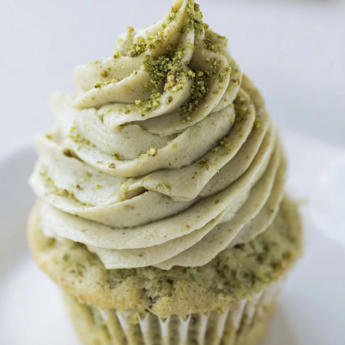 Golden pistachio cupcakes with fluffy nutty frosting, garnished with crushed pistachio bits
