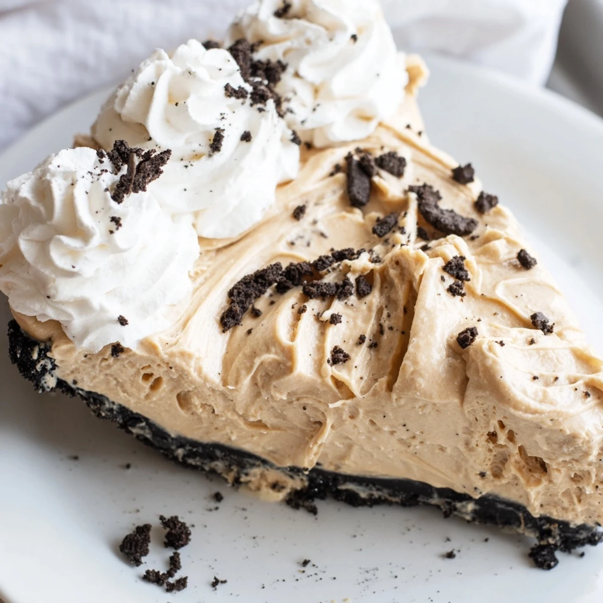 Creamy peanut butter Oreo pie sliced and topped with whipped cream and cookie crumbles