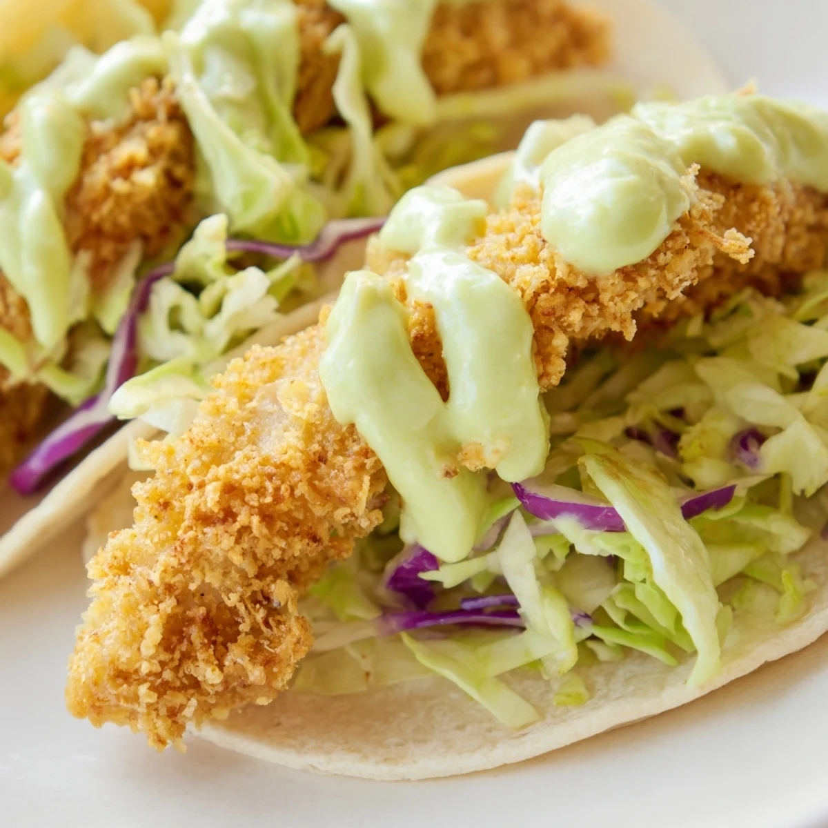 Golden crispy Baja fish tacos topped with fresh cabbage slaw and creamy avocado crema drizzle