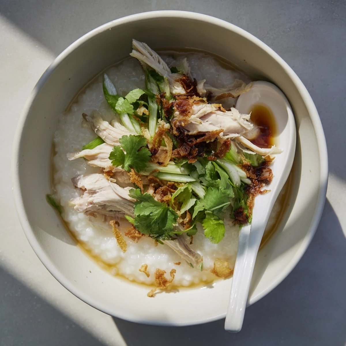 Creamy chicken congee topped with fresh scallions and drizzled with sesame oil in a white bowl