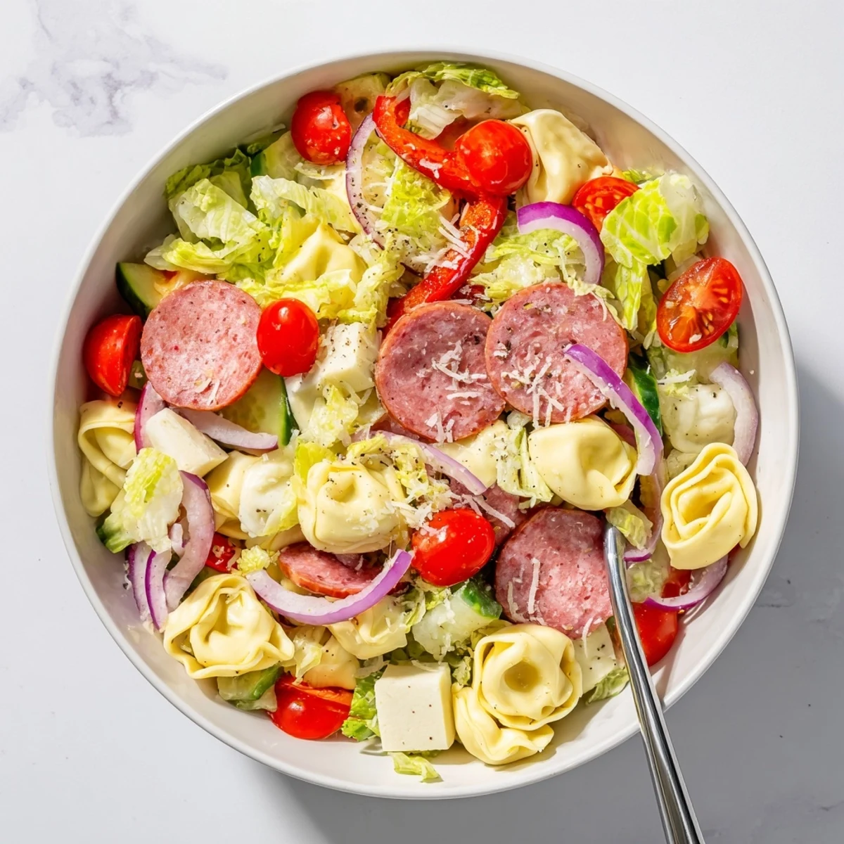 Vibrant Italian grinder pasta salad featuring cheesy tortellini cubes, red onion, and shredded lettuce topped with grated Parmesan