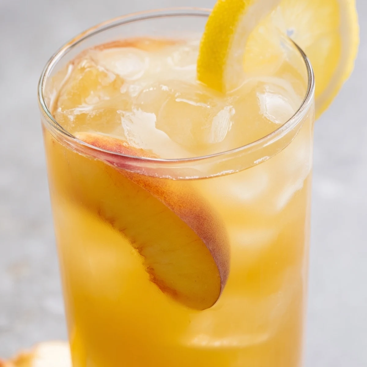Golden peach lemonade pitcher filled with floating peach slices and ice cubes for summer