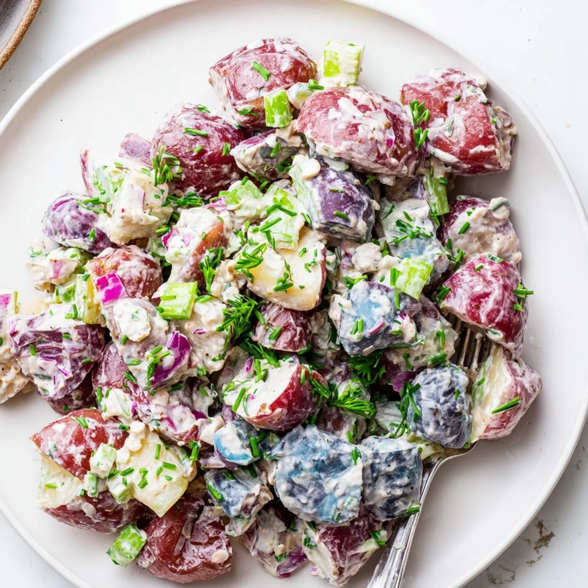 Creamy Red White Blue Potato Salad with diced celery on a sunny picnic table